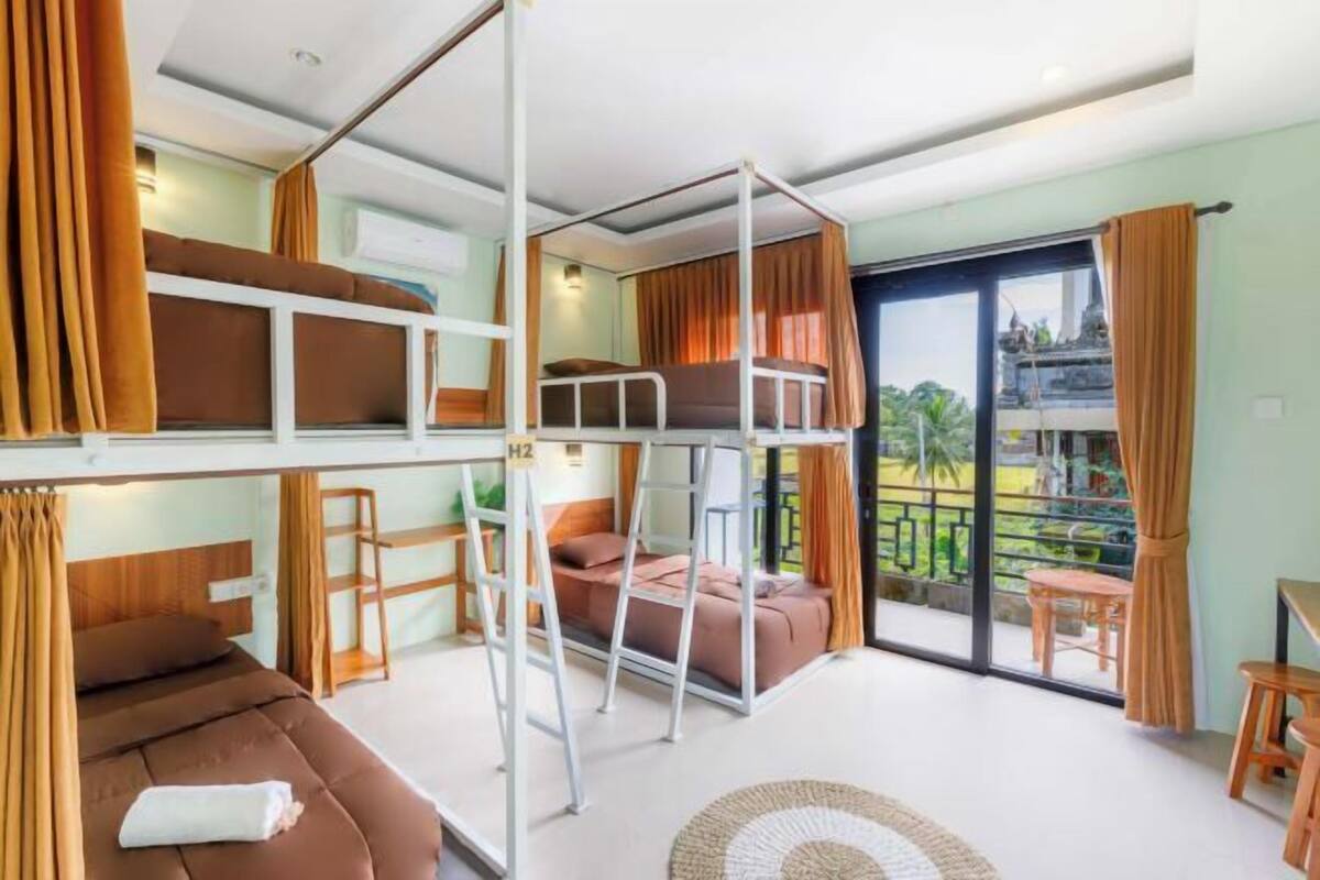 A room with bunk beds, a sofa, a small table, and a balcony with curtains.