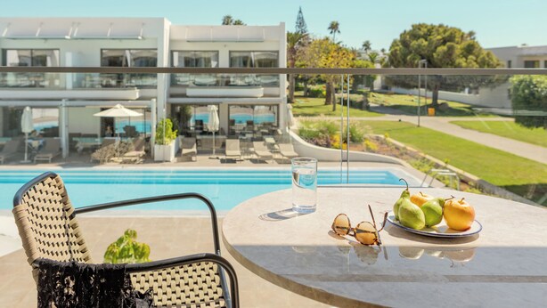Un balcon donnant sur la piscine, une table avec des fruits et un verre d’eau, et une chaise.