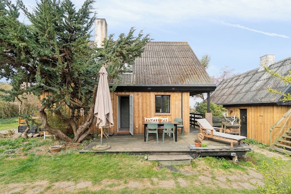 A wooden cabin with a deck, a table with chairs, and a lounge chair.