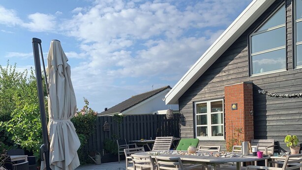 Eine Holzterrasse mit Tisch und Stühlen, einem beschatteten Sonnenschirm und Kübelpflanzen.