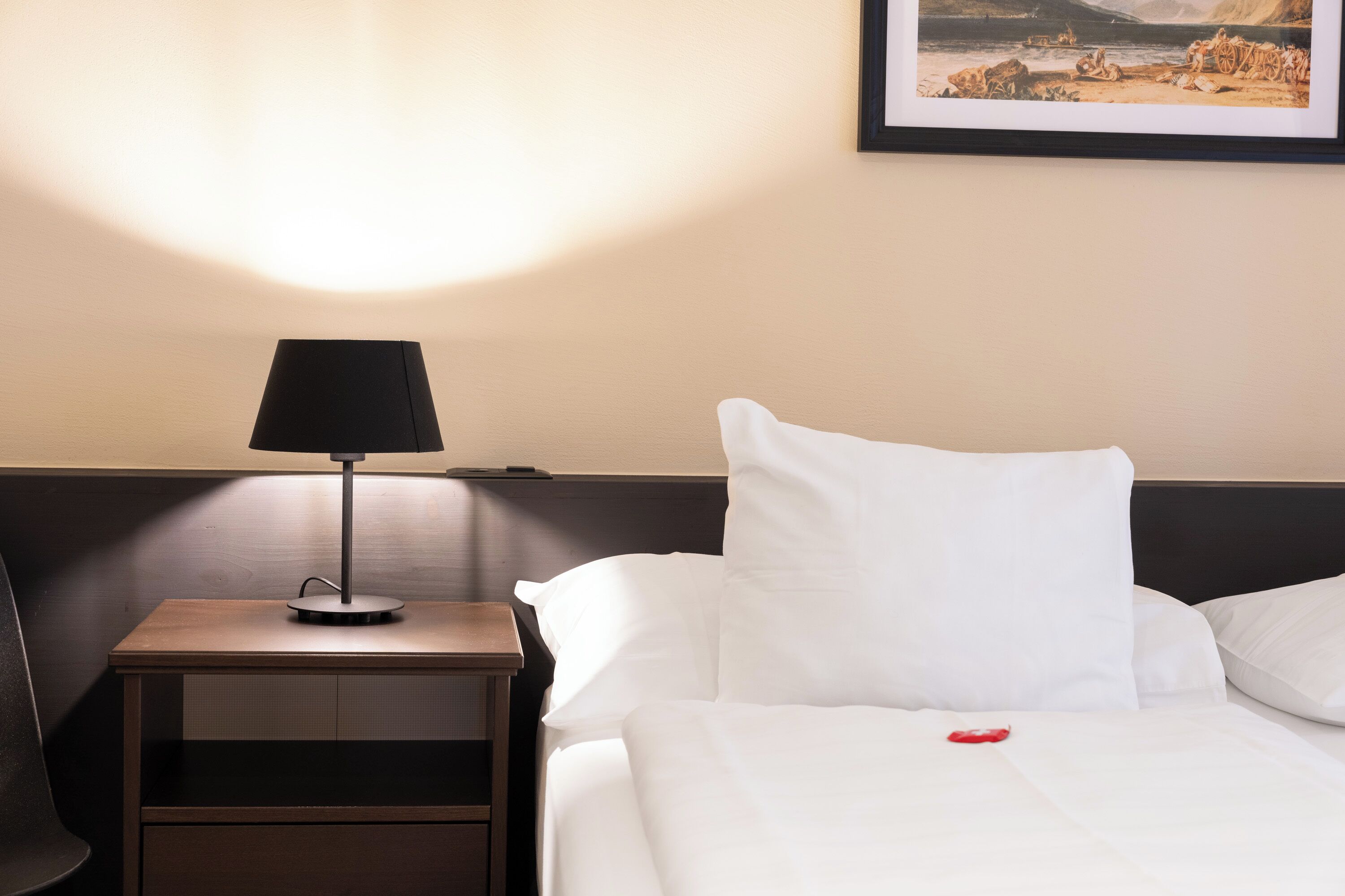 Una habitación de hotel con una cama bien hecha, una mesita de noche con lámpara y un cuadro en la pared.
