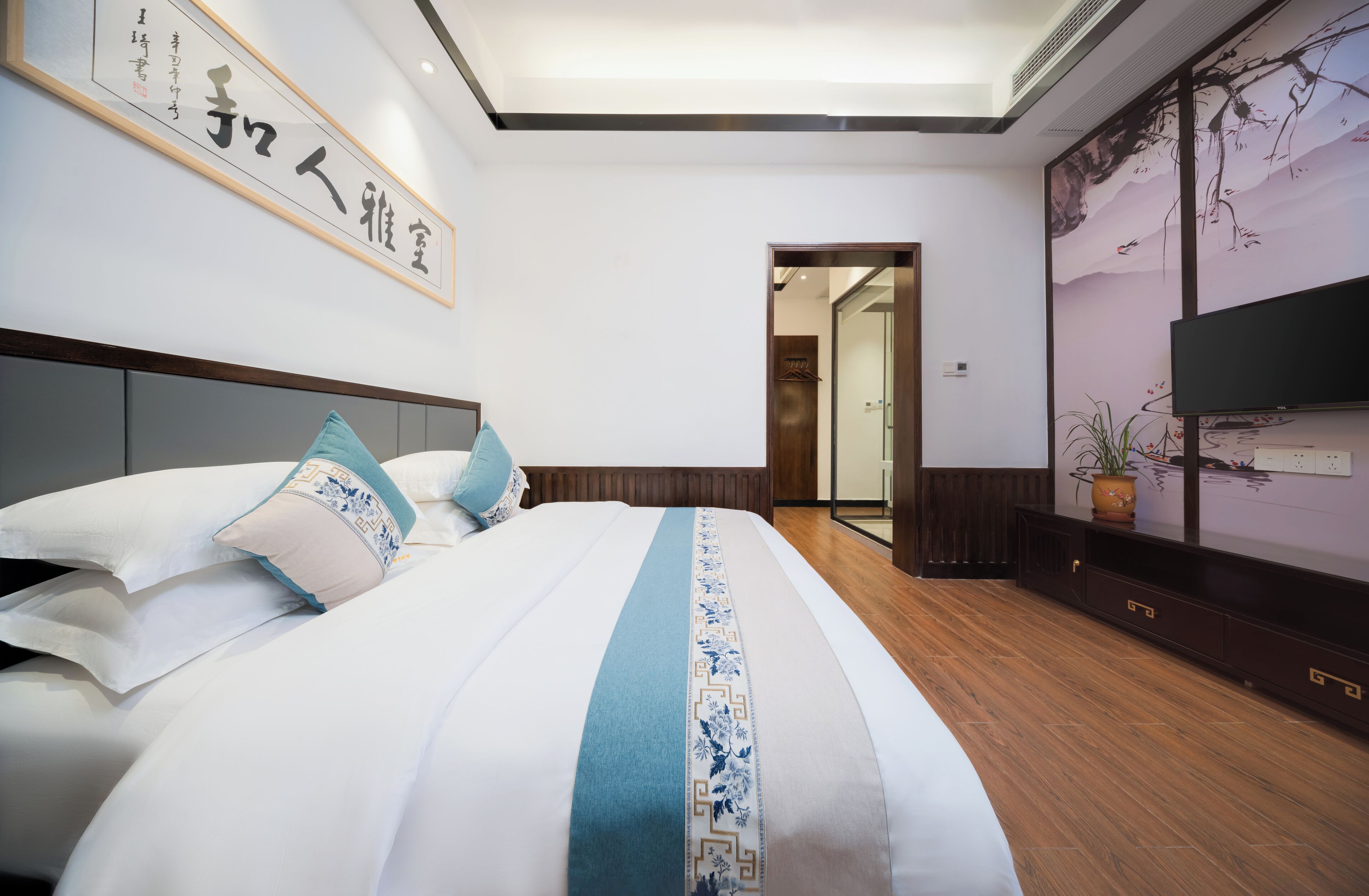 A hotel room with a large bed, a television, a wardrobe, and a framed artwork on the wall.