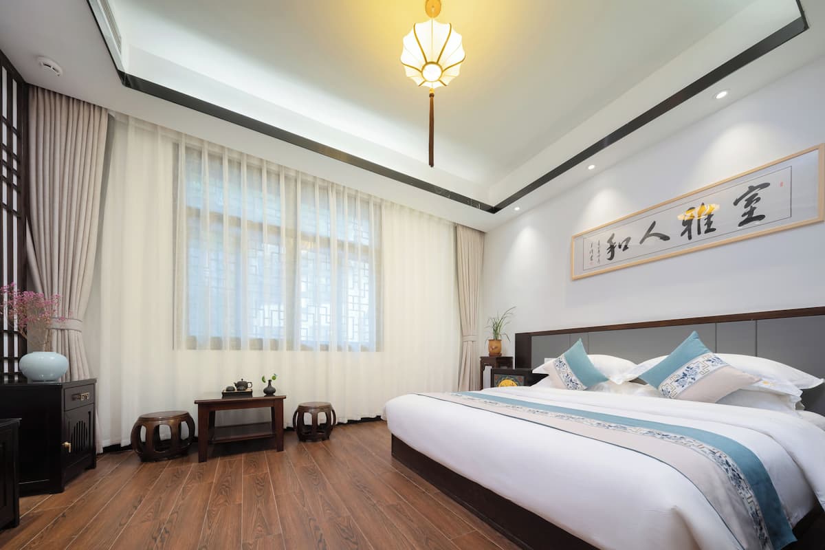 Una habitación de hotel moderna con una cama grande, suelo de madera, una lámpara en el techo y una obra de arte colgada en la pared.