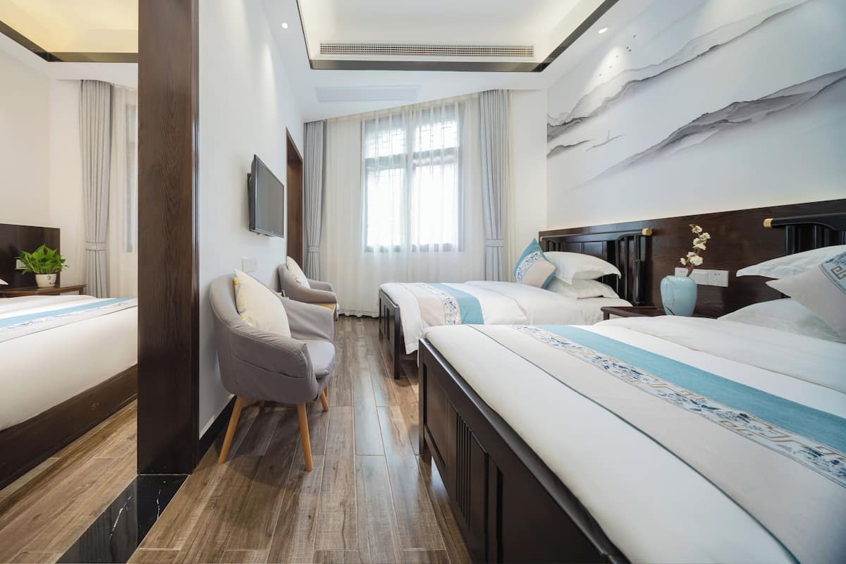 Habitación de hotel con una cama grande, una cama más pequeña, un sofá, un televisor y una ventana con cortinas.