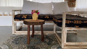 A rustic sofa with patterned cushions, a wooden side table with a vase of flowers, and a patterned rug on a concrete floor. - MUMBI VILLA WATAMU (Watamu)