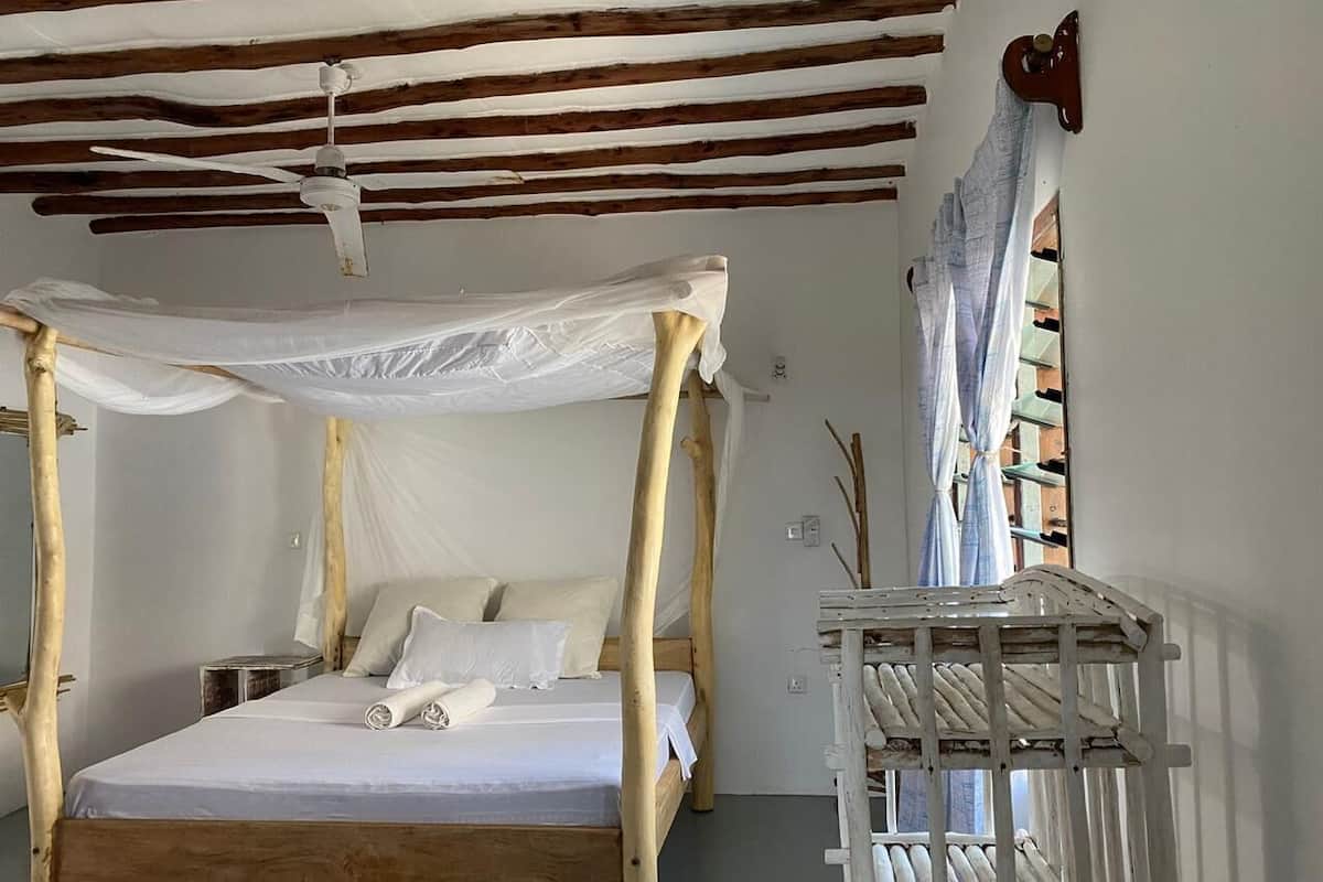 A bed with a canopy, wooden beams on the ceiling, and a window with curtains.