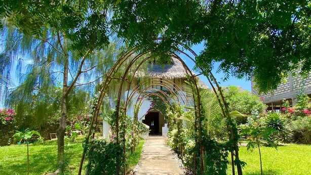 A garden pathway leading to a gazebo with a thatched roof, surrounded by lush greenery and flowering plants. - MUMBI VILLA WATAMU (Watamu)