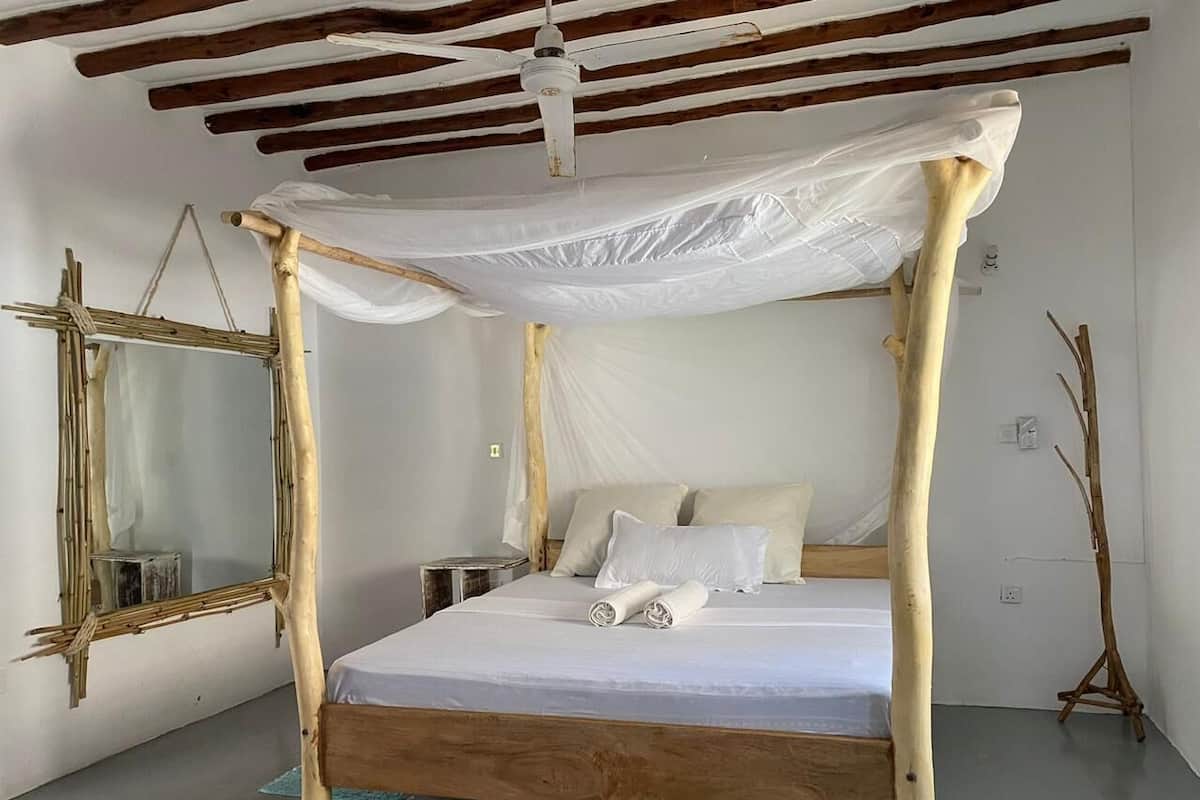 A room with a bed under a canopy, a wooden-framed mirror, and a standing lamp.