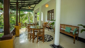 A covered outdoor seating area with tables and chairs, a bench, and potted plants. - Sleeperwood Villa (Unawatuna)