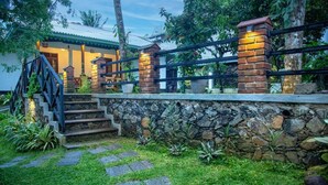 A stone wall with a metal railing, a staircase, and a well-maintained garden with stepping stones. - Sleeperwood Villa (Unawatuna)