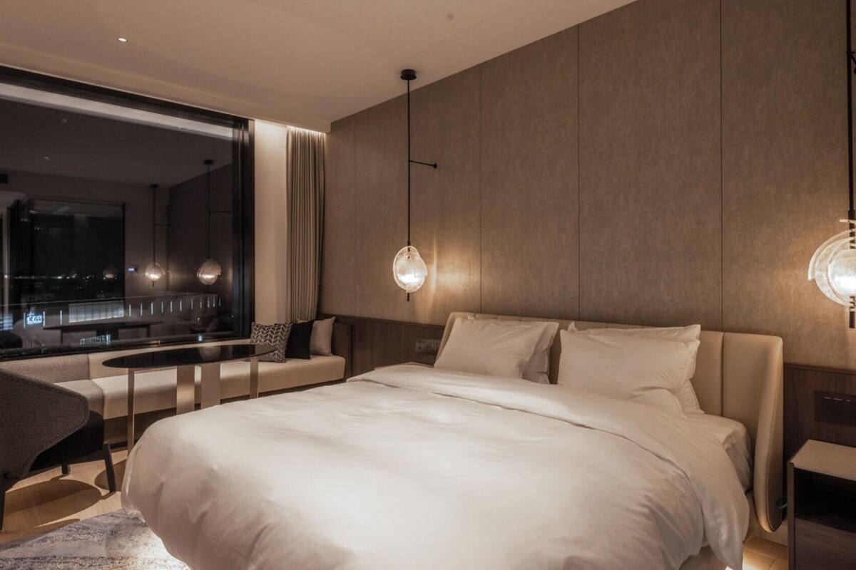 A modern hotel room with a large bed, a seating area with a view, and two pendant lights.