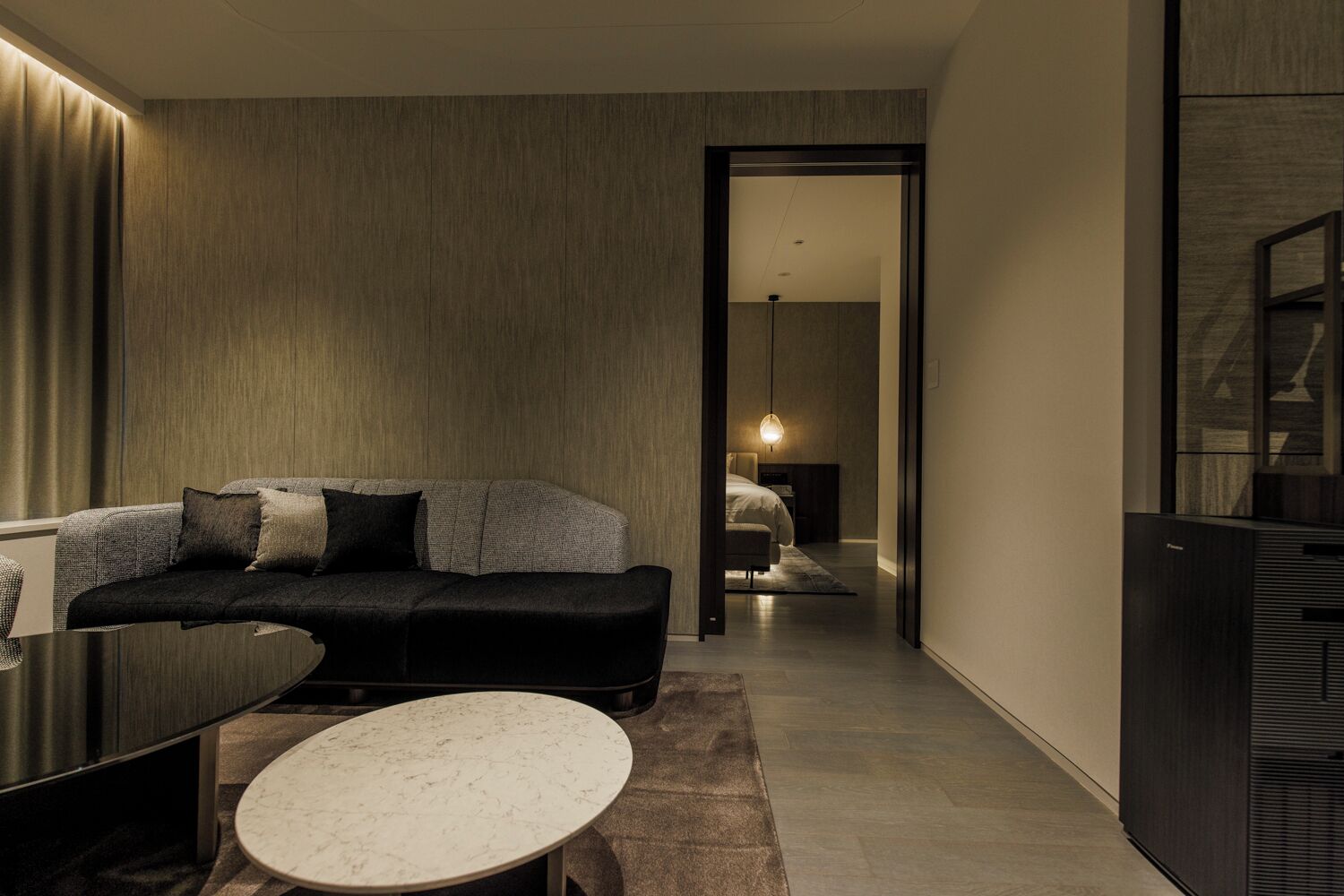 A modern hotel room with a sofa, a round table, and a bed in the background.