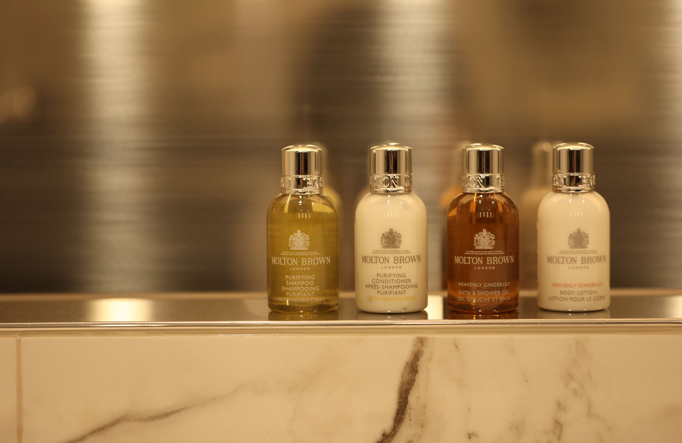 Vier flessen Molton Brown producten op een marmeren aanrecht.