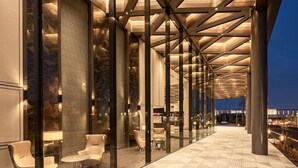A modern hotel corridor with glass walls, seating areas, and a geometric patterned floor. - ATAGO HOTEL (Noda)