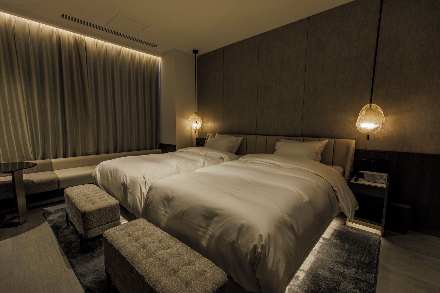 Una habitación de hotel moderna con dos camas, un sofá, una mesita y un banco.