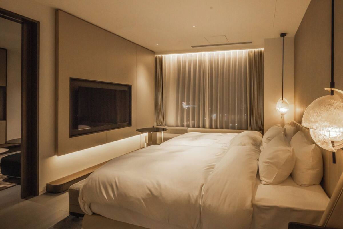 A modern hotel room with a large bed, a flat-screen TV mounted on the wall, a bedside table, and a unique spherical lamp.