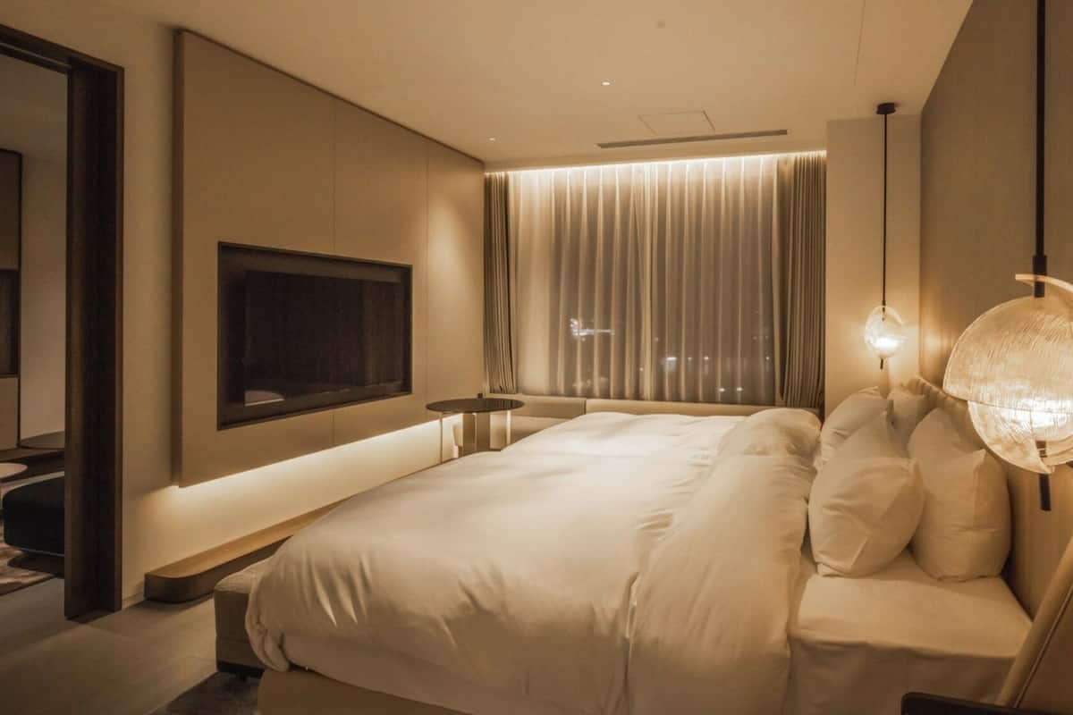 Ett modernt hotellrum med en stor säng, en platt-TV som är monterad på väggen, ett sängbord och en unik, sfärisk lampa.