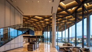 A spacious lobby with a high ceiling, a central staircase, and a seating area with sofas. - ATAGO HOTEL (Noda)