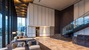 A spacious lobby with a high ceiling, a staircase, and a seating area with sofas. - ATAGO HOTEL (Noda)