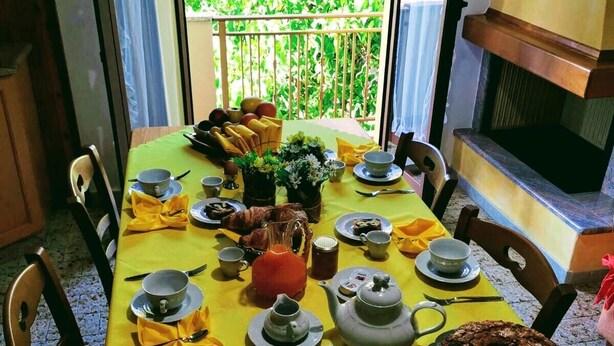 A dining table set with yellow tablecloth, plates, cups, and a teapot, with a view of greenery outside. - B&B the bikers (Guspini)