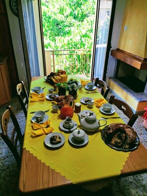 A dining table set with yellow tablecloth, plates, cups, and a teapot, with a view of greenery outside. - B&B the bikers (Guspini)