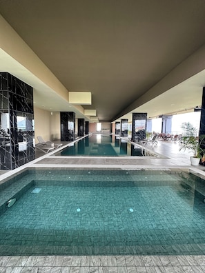 A large indoor swimming pool with clear water, surrounded by lounge chairs and a modern interior design. - ICC Luxury Suites Ipoh City Centre (Ipoh)