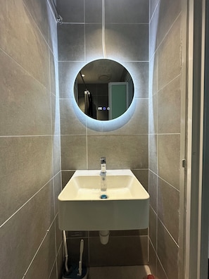 A bathroom with a round mirror, a sink, and tiled walls. - ICC Luxury Suites Ipoh City Centre (Ipoh)
