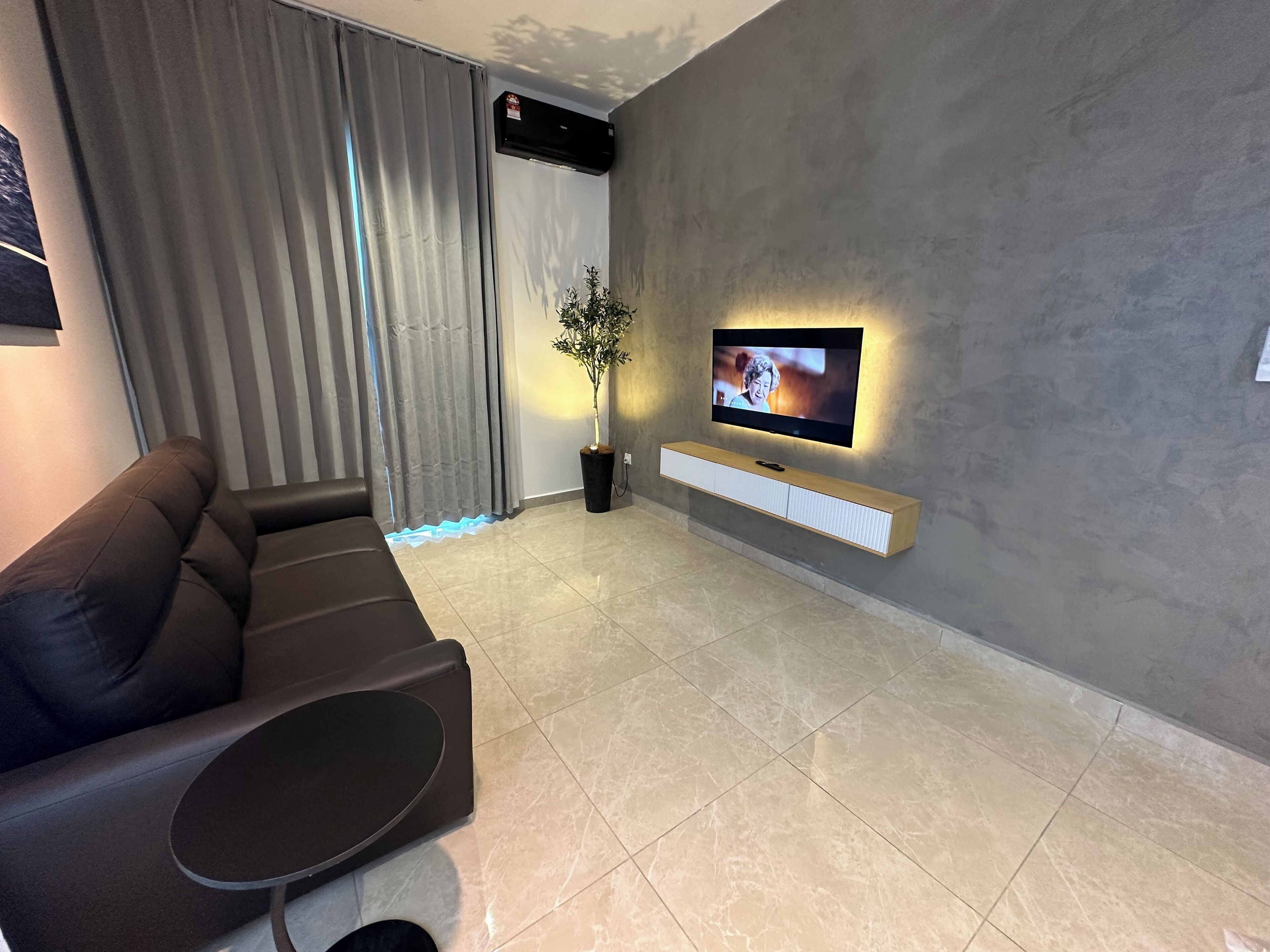 A modern living room with a sofa, a TV mounted on the wall, and a potted plant.