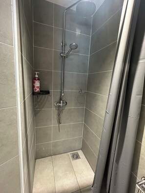 A shower with a handheld showerhead and a wall-mounted faucet. There is a small shelf with a bottle of shampoo. - ICC Luxury Suites Ipoh City Centre (Ipoh)