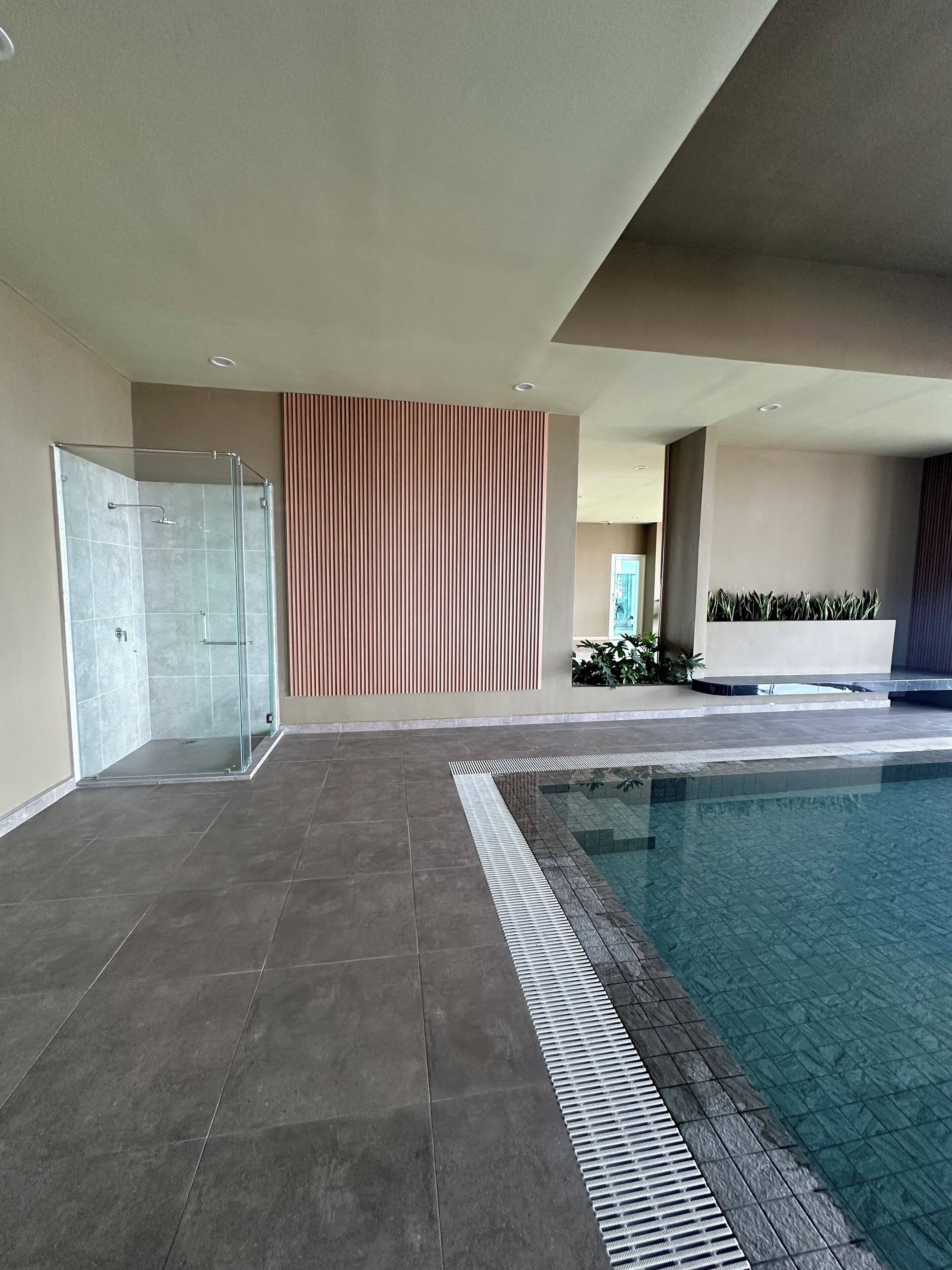 A modern indoor pool area with a glass-enclosed shower, tiled flooring, and a decorative wall with vertical lines.