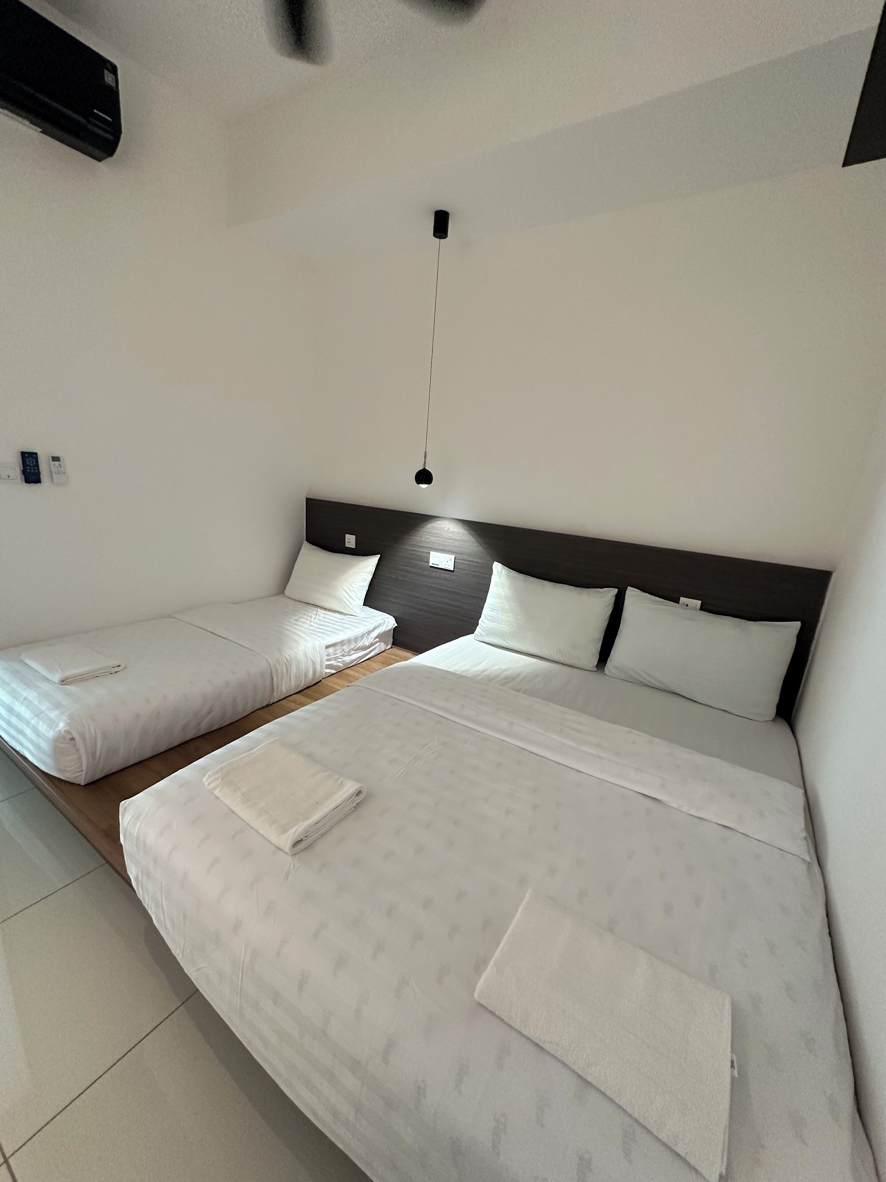 Ett hotellrum med två sängar, en sänggavel i trä och en hängande lampa.