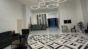 Moderni aula, jossa on geometrisesti kuvioitu lattia, vastaanottotiski, oleskelualue ja pyöreillä valaisimilla varustettu katto.