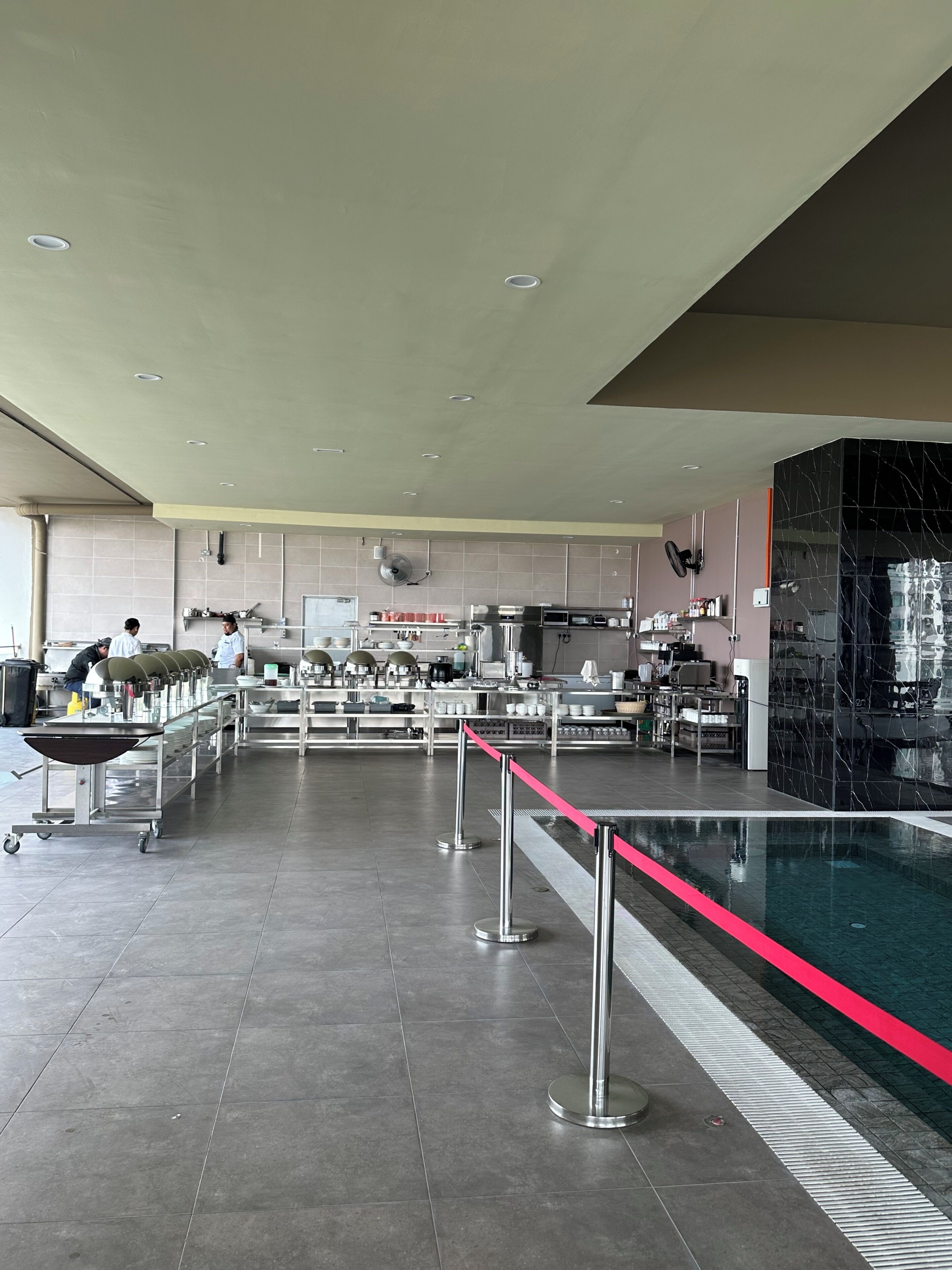 A spacious kitchen area with stainless steel appliances, a long counter, and a red safety line near a pool.