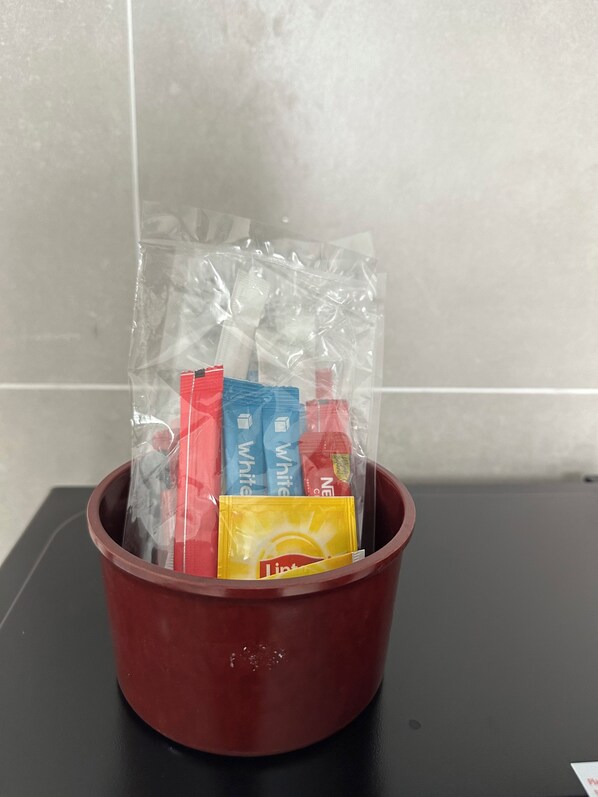A brown bucket containing various toiletries, including a yellow bottle labeled 'Lindt' and several packets of 'White' and 'Red' products. - ICC Luxury Suites Ipoh City Centre (Ipoh)