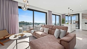 A modern living room with a large sofa, a coffee table, and a view of the city through large windows.