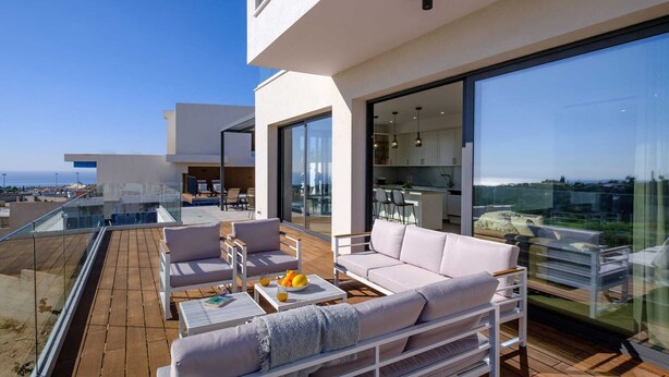 A modern outdoor living area with a wooden deck, white furniture, and a glass balustrade.
