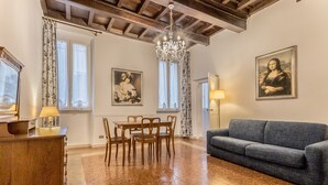 A spacious living room with a wooden dining table, a blue sofa, and two paintings on the walls. - Casa Iside in Rome With 1 Bedrooms and 1 Bathrooms (Rome)