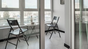 Una habitación moderna con ventanas amplias, dos sillas, una mesita y una botella.