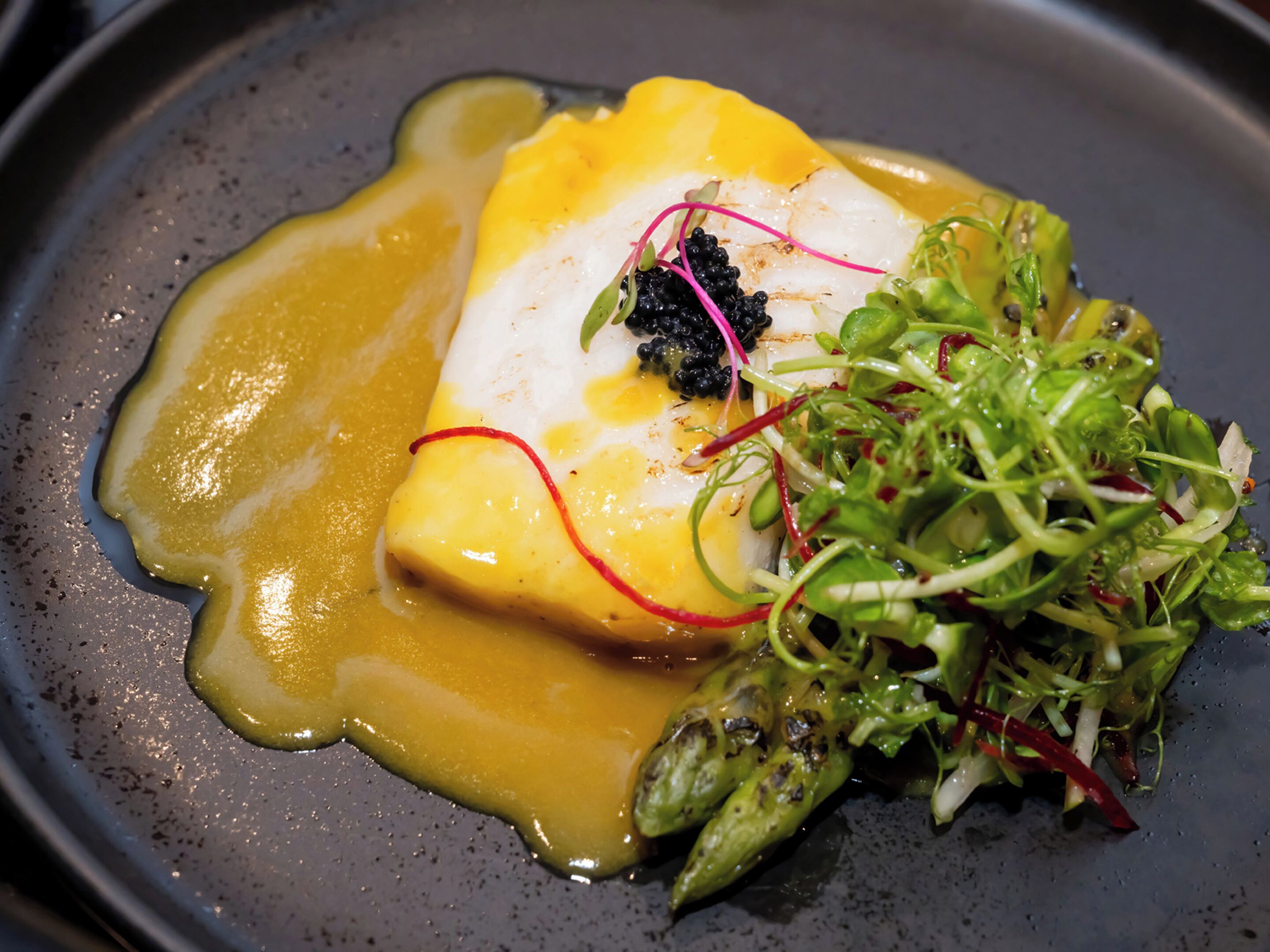 A dish with a creamy sauce, a poached egg, and garnishes including microgreens and caviar.
