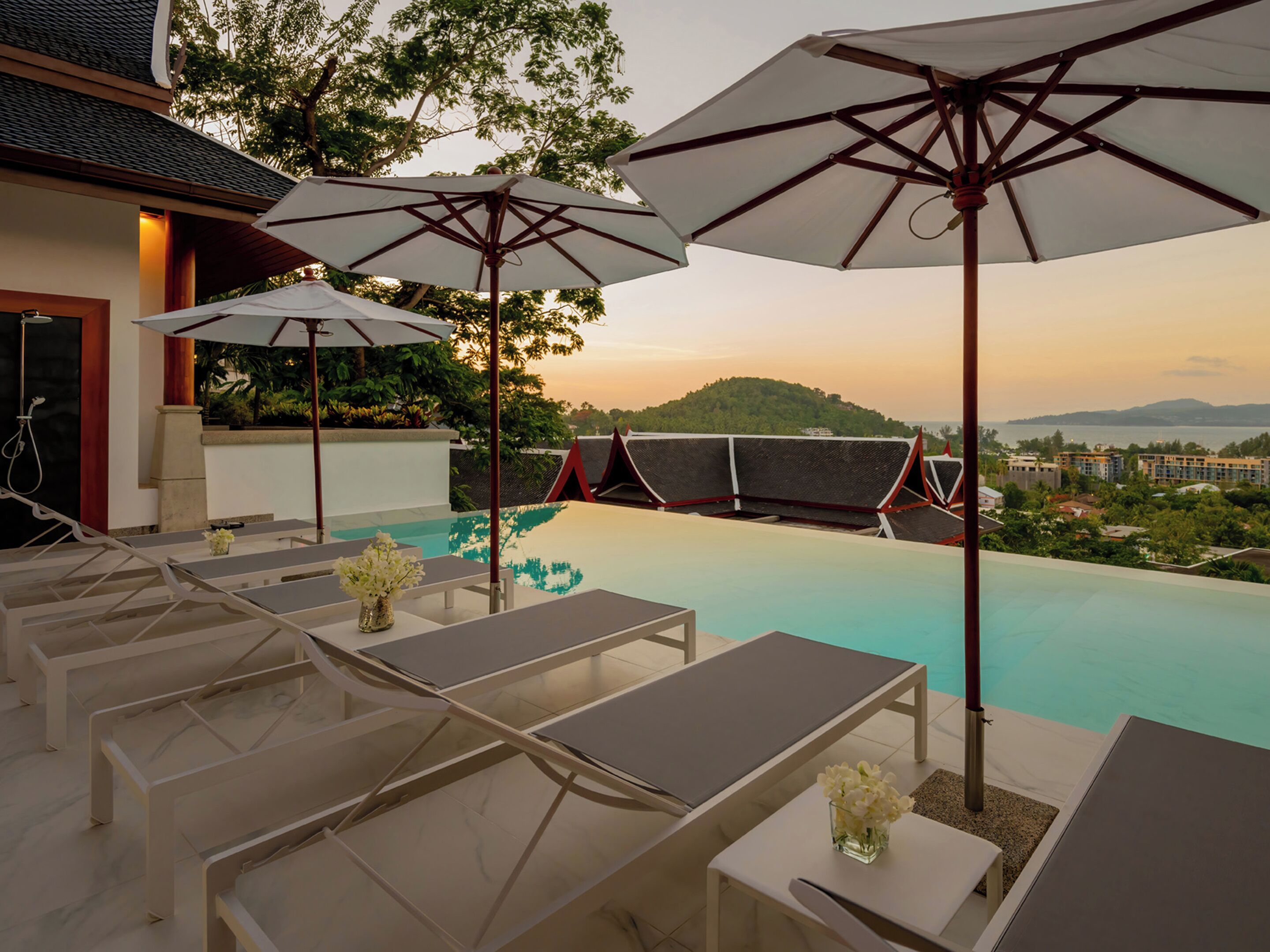 Una piscina infinita con sillones de descanso y sombrillas, con vistas a un paisaje pintoresco de colinas y una masa de agua.