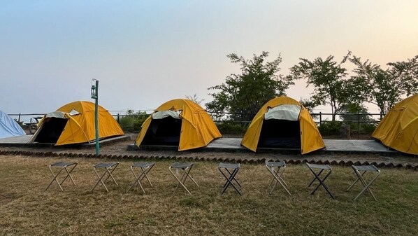 A row of yellow tents with a metal railing in the foreground and trees in the background. - Kunjapuri camps (Rishikesh)