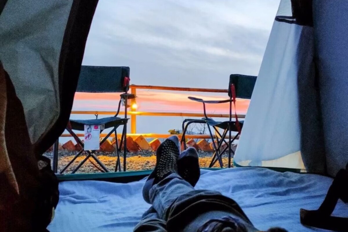 A tent with a view of a sunset, a bed, and two chairs.