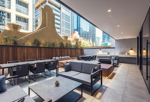 Relax in this stylish space with a long dining table, sofa, and coffee table, surrounded by a unique architectural sculpture and large windows offering a city view.