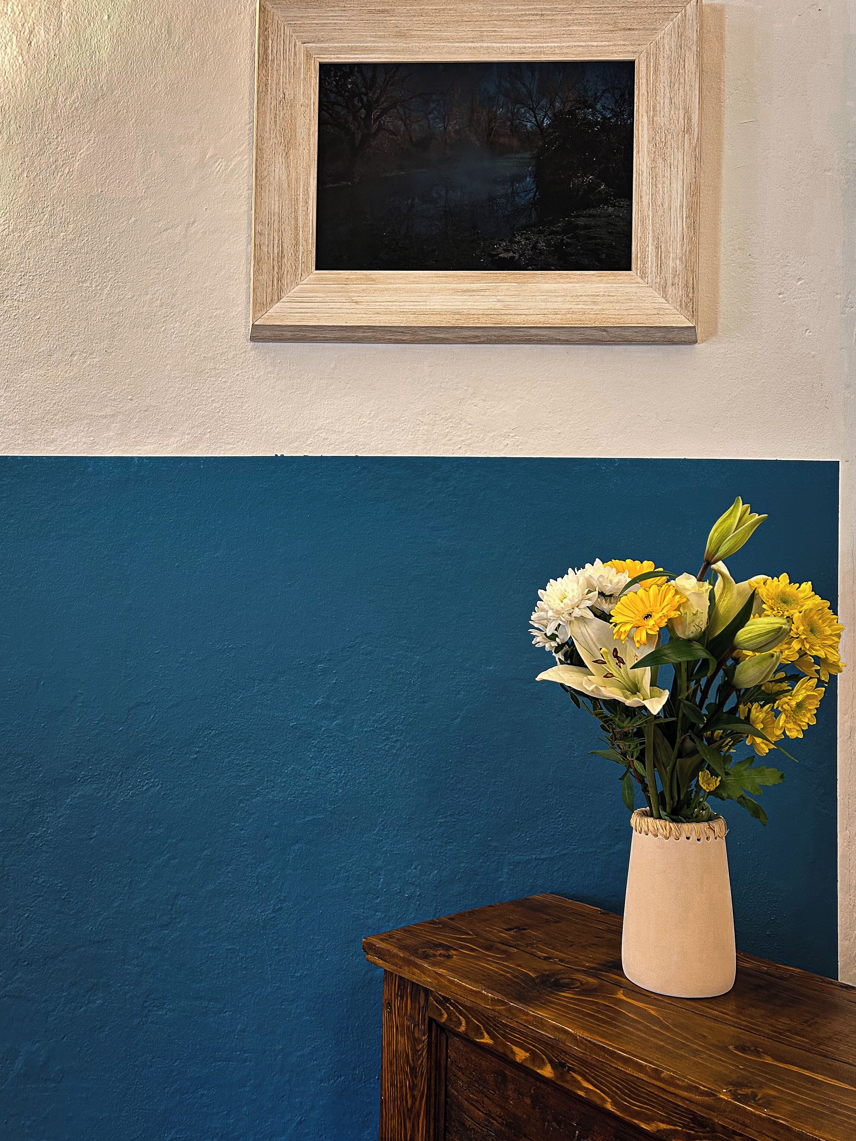 A room with a blue and white wall, a wooden table, and a vase with flowers.