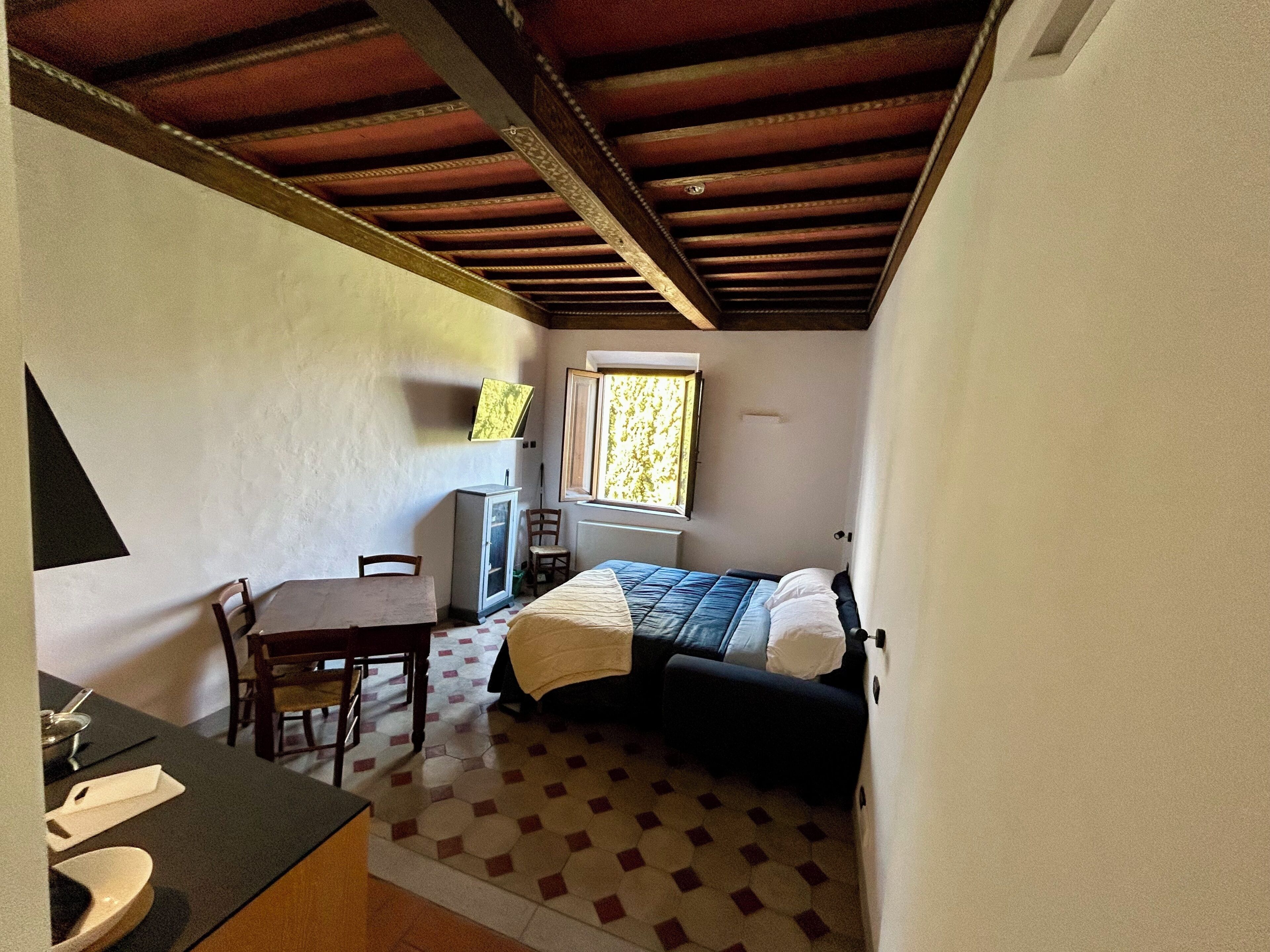 A small, cozy room with a bed, a desk, and a chair. There is a window with a view of trees.
