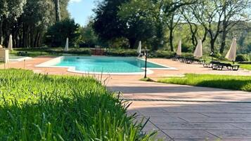Una piscina con un borde empedrado, rodeada de césped y árboles.