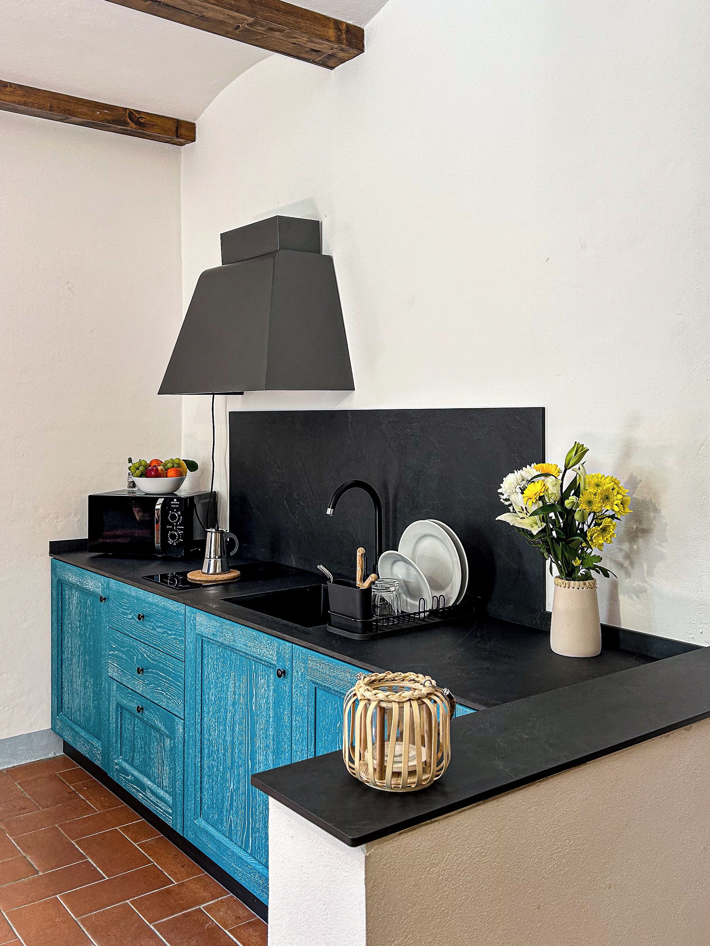 A kitchen with a black countertop, a blue cabinet, a black sink, and a vase with flowers.