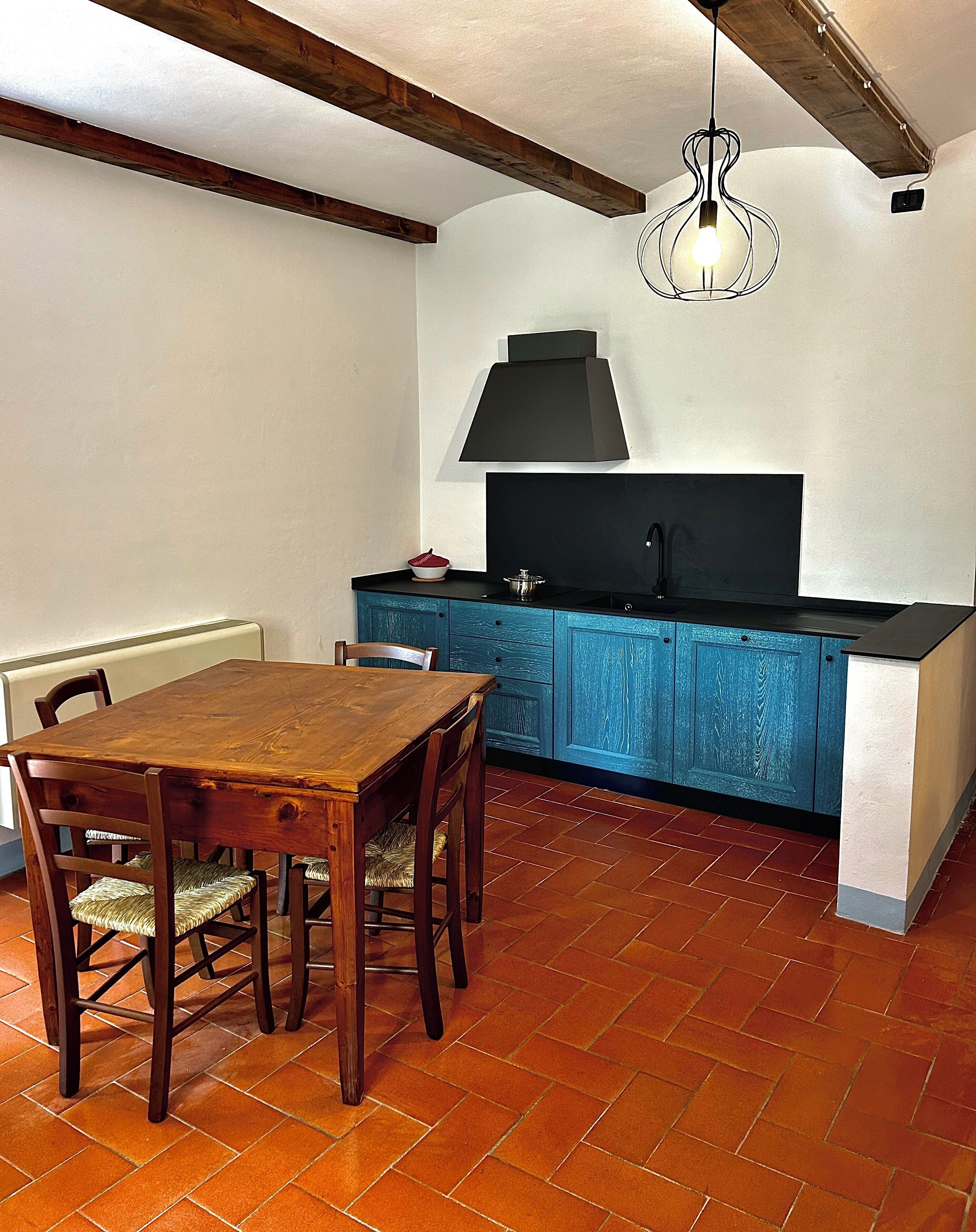 Una cocina con una mesa y sillas de madera, un armario azul y una campana extractora negra.