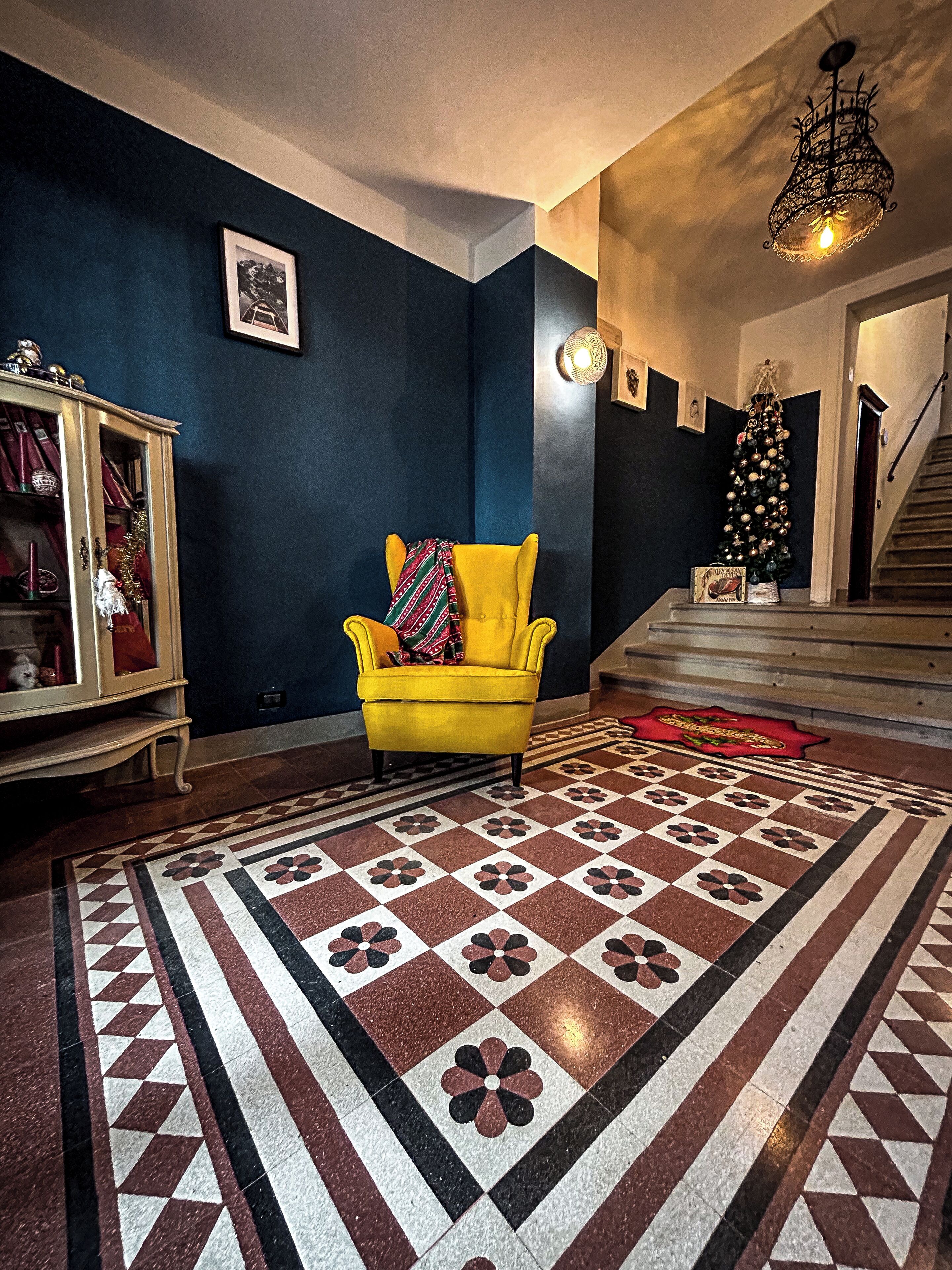 Uma sala de estar com piso estampado, uma poltrona amarela, uma árvore de Natal e uma escada.