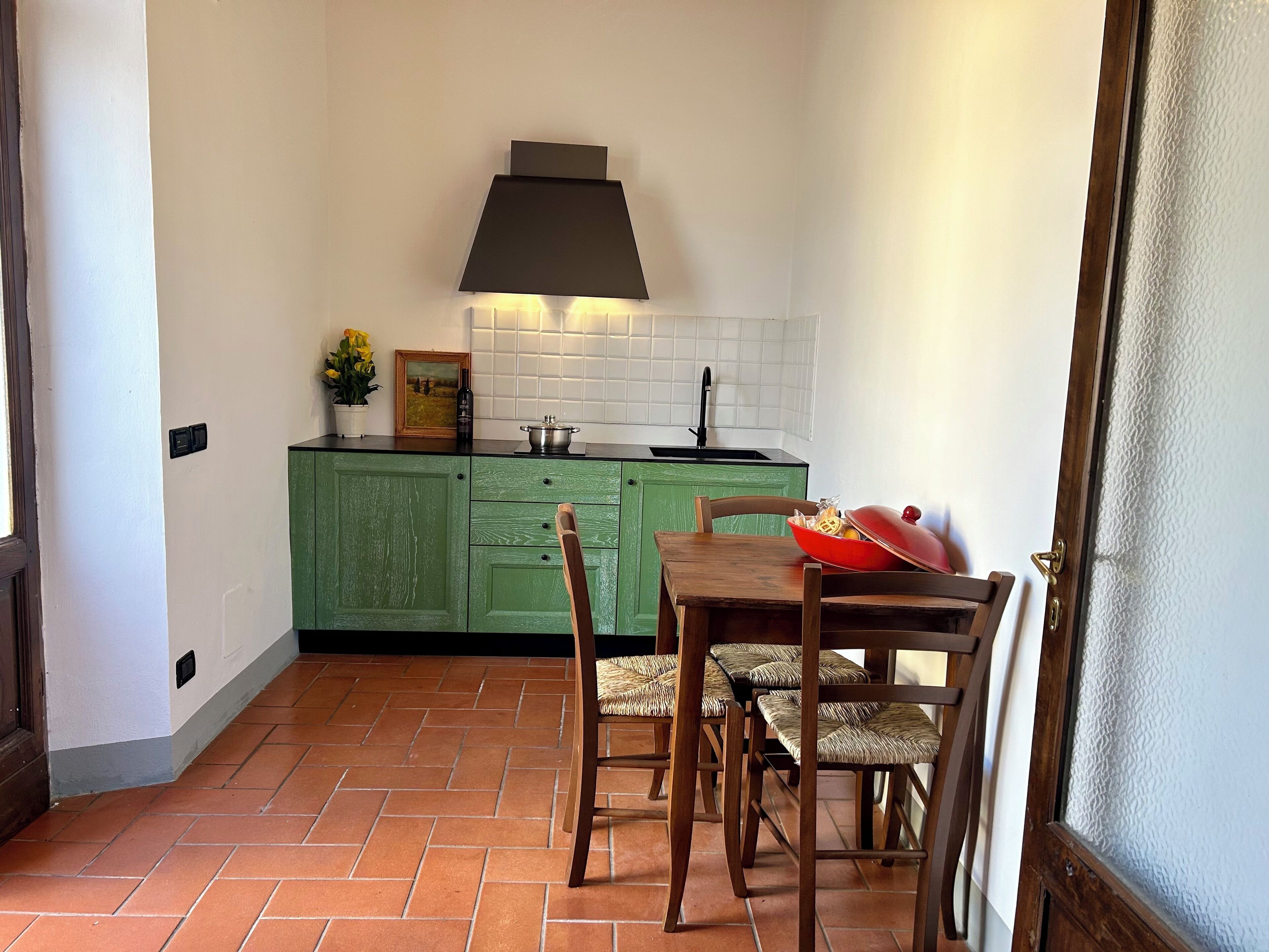 Una cocina compacta con gabinetes verdes, una campana extractora negra y un salpicadero de azulejos.